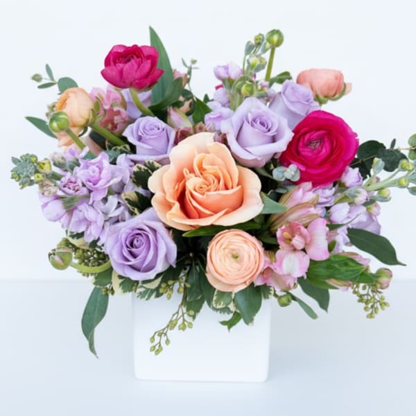 Mixed pastel bouquet in a white vase with peach, lavender, and pink blooms