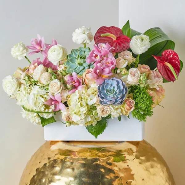 Mixed floral arrangement in a white container on a gold vase
