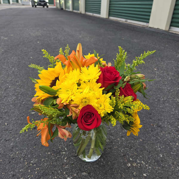 Bouquet of red roses, yellow daisies, and orange lilies in a glass vase