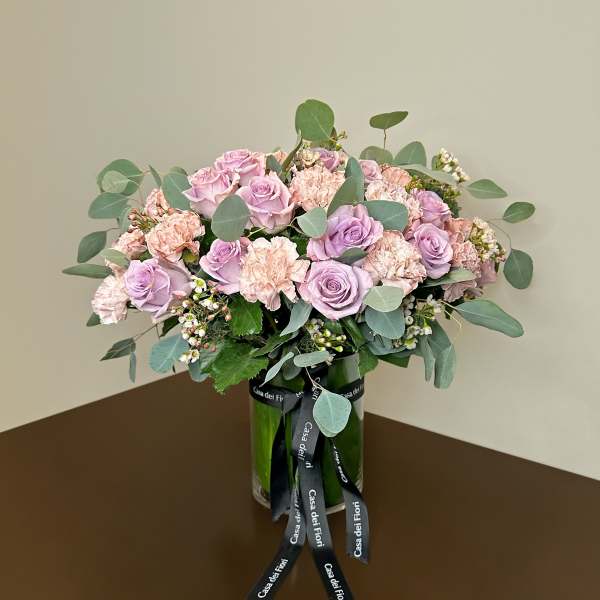 Pink roses and carnations arranged in a glass vase with a ribbon