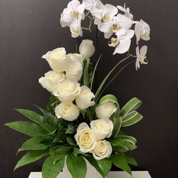 White roses and orchids arranged in a white vase