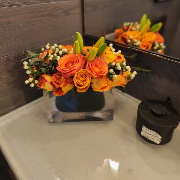 Orange roses and lily buds arranged in a low square vase