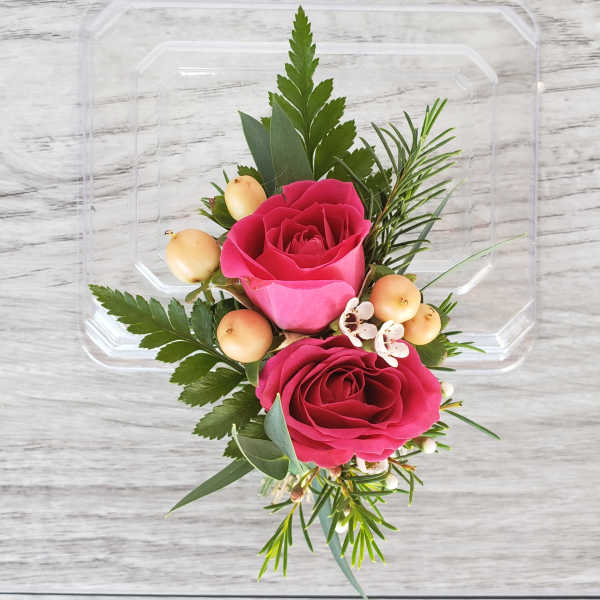 Two pink roses with berries in a clear plastic container