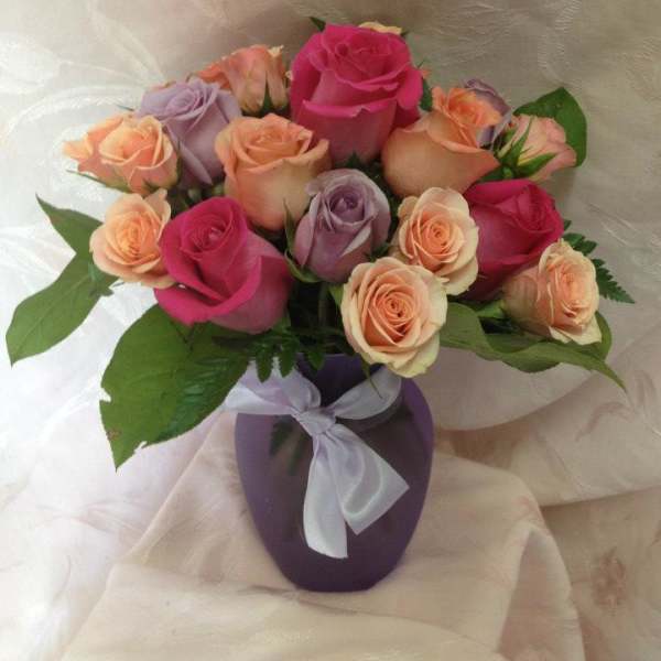 Bouquet of pink, peach, and lavender roses in a purple vase with a ribbon
