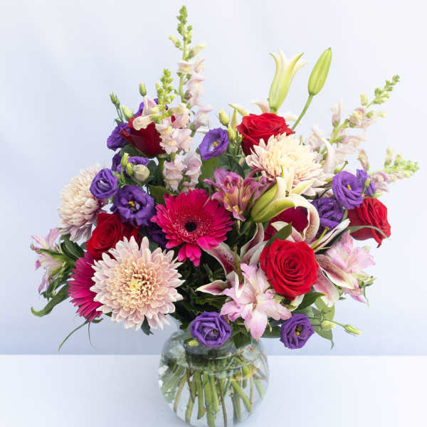 Mixed bouquet of red, purple, and pink flowers in a glass vase