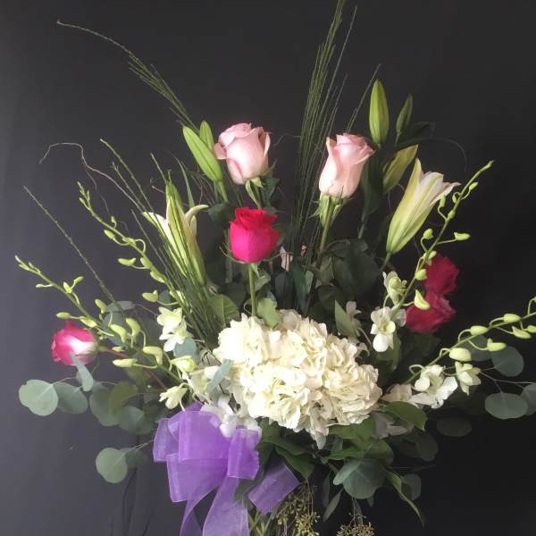 Tall bouquet of pink roses, white lilies, and white hydrangeas in a glass vase