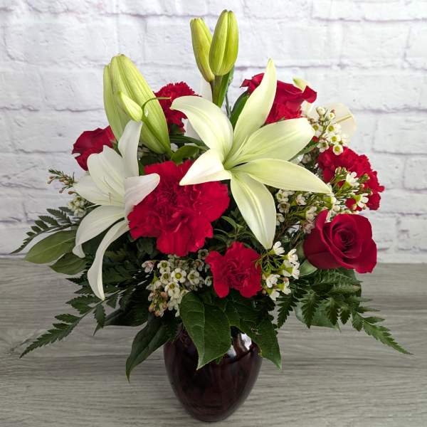 Bouquet of white lilies, red roses, and red carnations in a dark glass vase