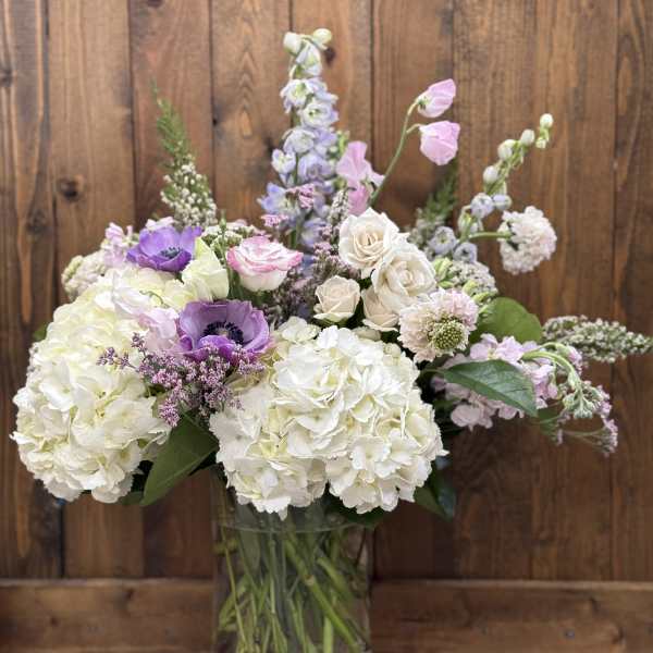 Bouquet of white hydrangeas, roses, and purple flowers in a glass vase