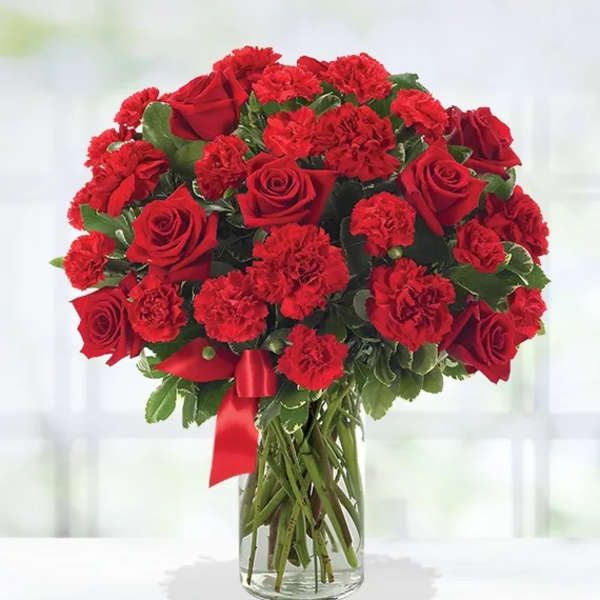 Red roses and carnations in a clear glass vase with a red ribbon
