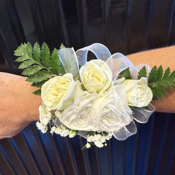 White rose wrist corsage with sheer ribbon accents worn on an arm.