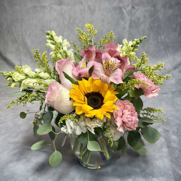Bouquet of sunflowers, pink alstroemeria, and carnations in a glass vase