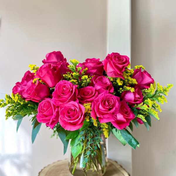 Pink rose bouquet in a clear glass vase with yellow filler flowers