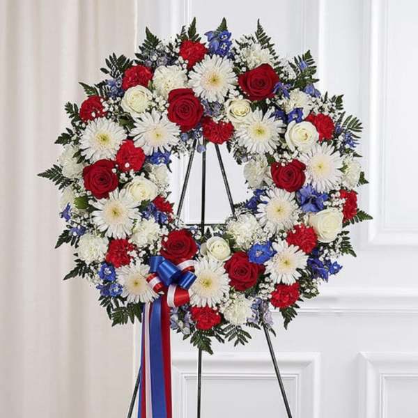 Red, white, and blue floral wreath on a black stand with ribbon