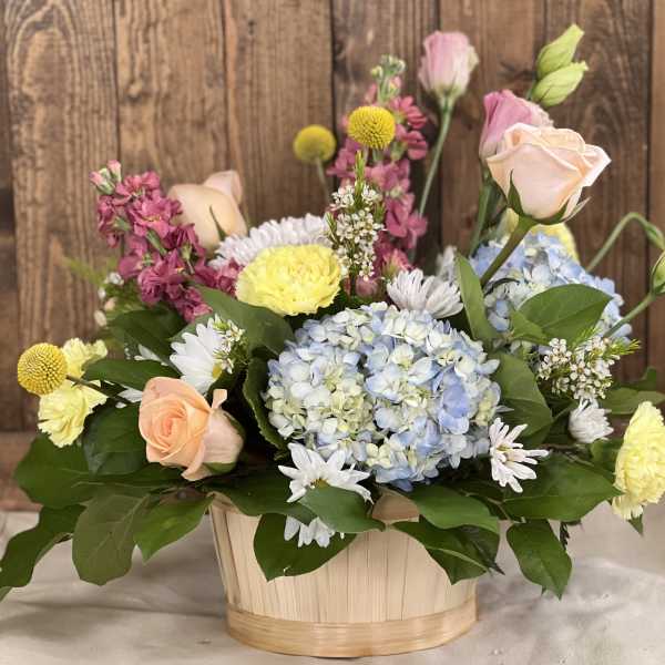 Mixed bouquet in a wooden basket with roses, hydrangea, and daisies