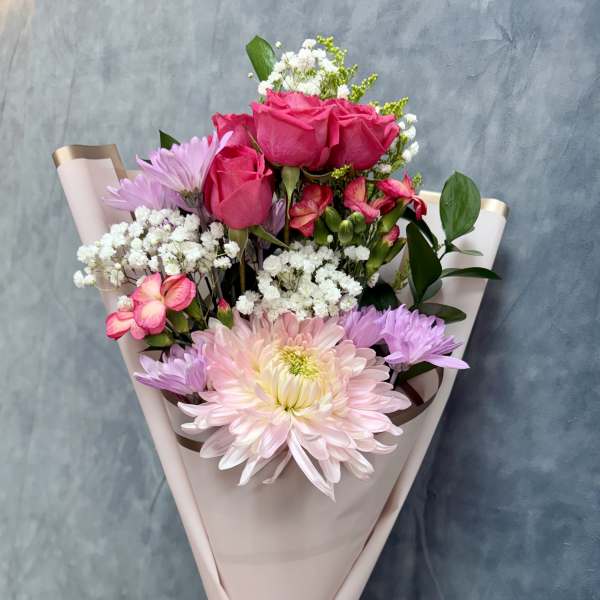 Bouquet of pink roses, daisies, and white filler flowers wrapped in blush paper