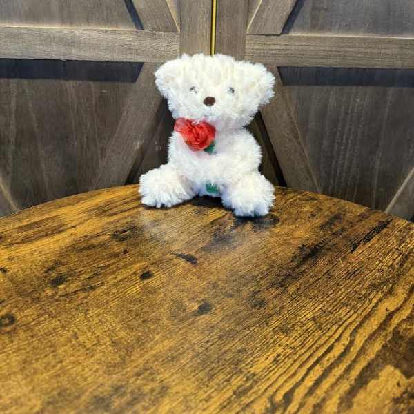 White teddy bear holding a red rose on a wooden table