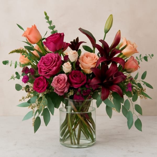 Mixed pink and peach roses with dark lilies in a glass vase