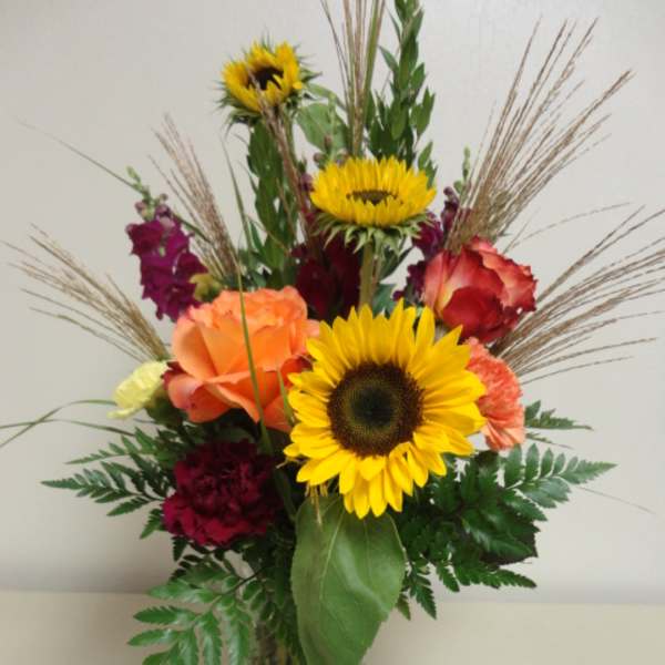 Mixed bouquet with sunflowers, roses, and carnations in a glass vase