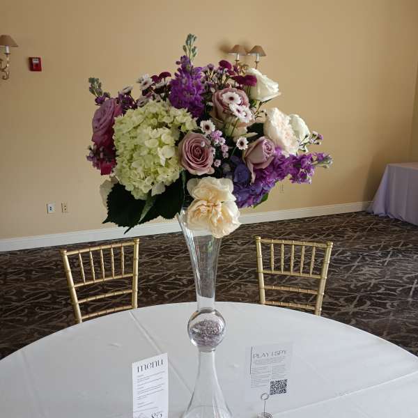 Tall floral centerpiece in a clear glass vase with purple, white, and blush blooms