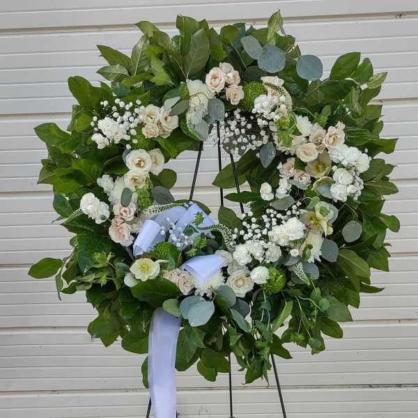 Large white floral wreath on a stand with a lavender ribbon