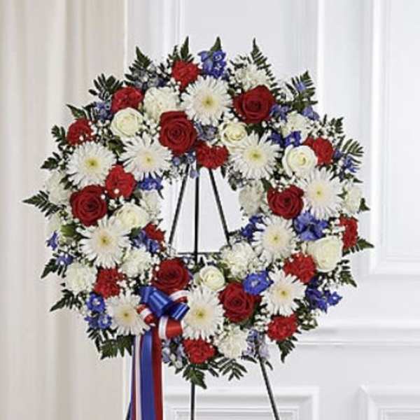 Red, white, and blue floral wreath on a black easel with ribbon