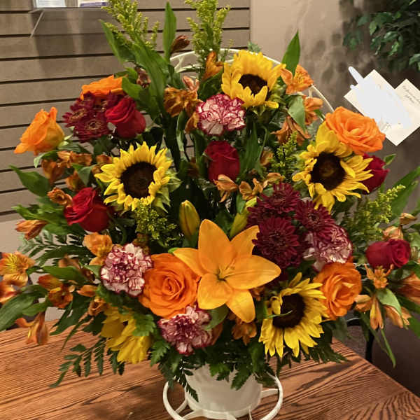Mixed bouquet in a white container with sunflowers, roses, and lilies