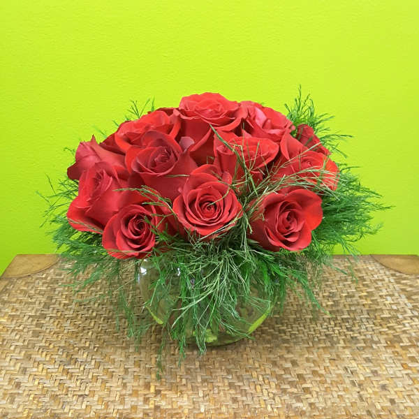 Red roses arranged in a low glass vase with airy greenery
