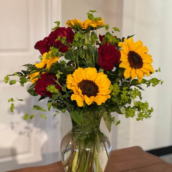 Red roses and yellow sunflowers arranged in a clear glass vase