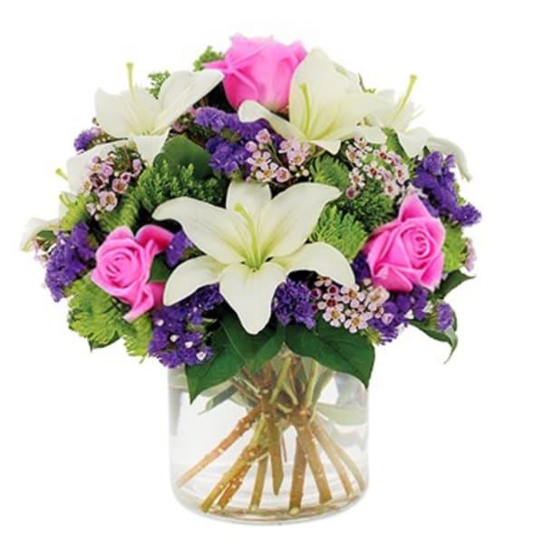 Bouquet of white lilies, pink roses, and purple filler in a clear glass vase