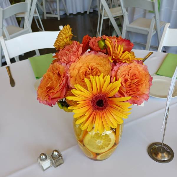 Orange and yellow flower arrangement in a glass vase with citrus slices