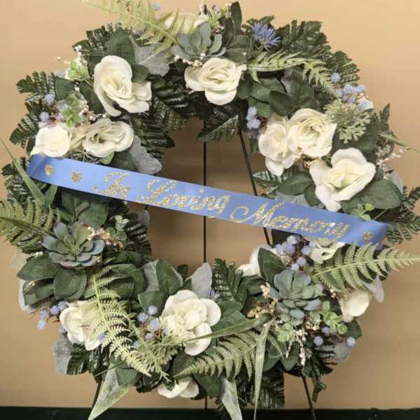 White floral memorial wreath with a blue ribbon on a stand