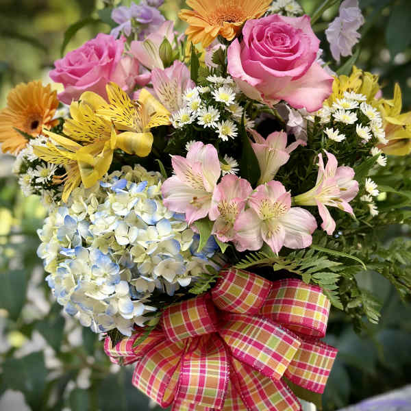 Mixed bouquet with pink roses, yellow flowers, and blue hydrangea in a glass vase