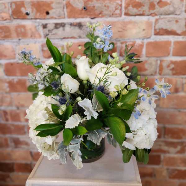 White floral arrangement with blue accents in a glass vase
