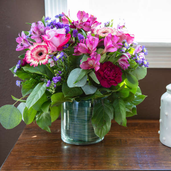Pink and purple mixed bouquet in a glass vase beside a white ceramic jar
