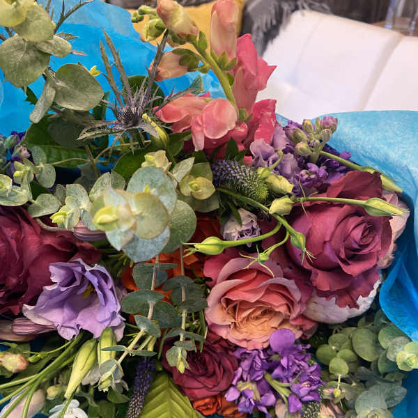 Mixed bouquet of pink, purple, and peach flowers wrapped in blue paper