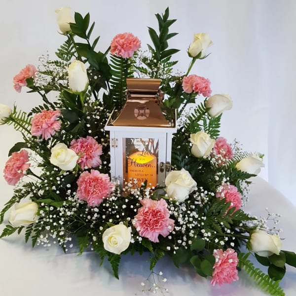White roses and pink carnations arranged around a lantern centerpiece