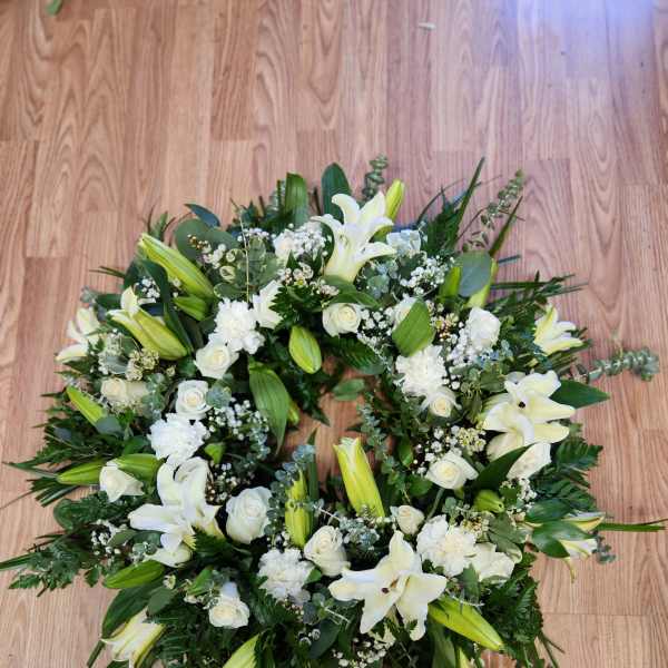 White floral wreath with lilies and roses on a wooden floor