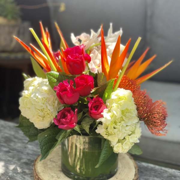 Bouquet of pink roses, white hydrangeas, and orange tropical blooms in a glass vase