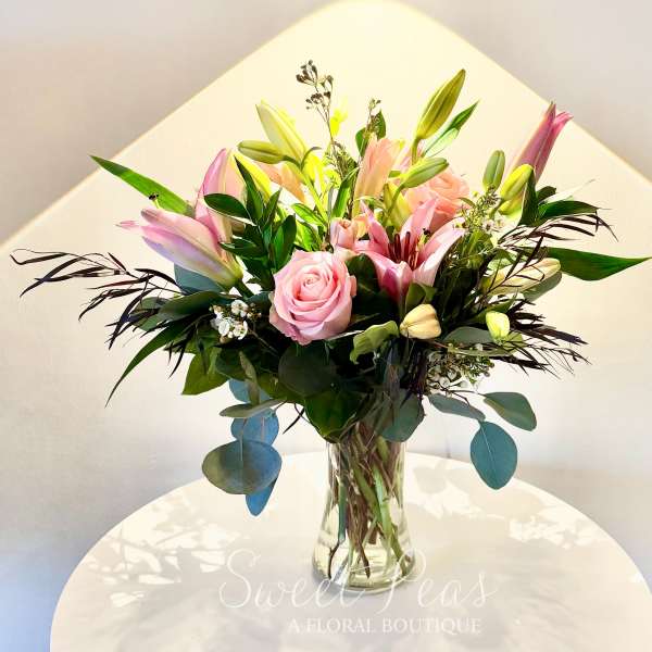 Pink lilies and roses with white accent blooms arranged in a clear glass vase.