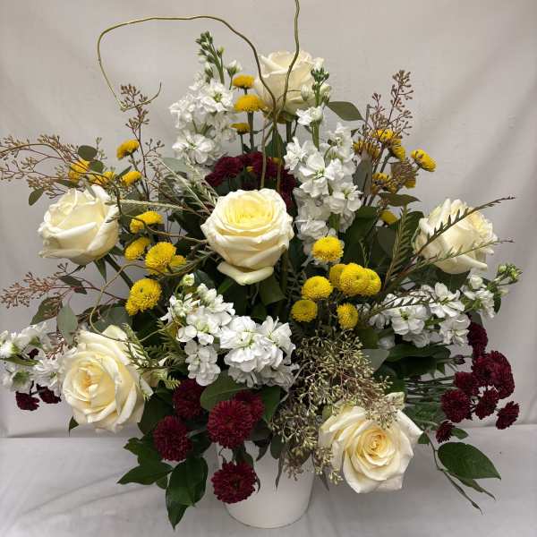 Tall arrangement of ivory roses, white stock, yellow button mums and burgundy mums in a white vase