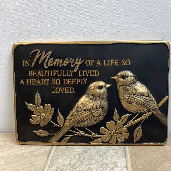 Memorial plaque with two birds and gold lettering on a black background