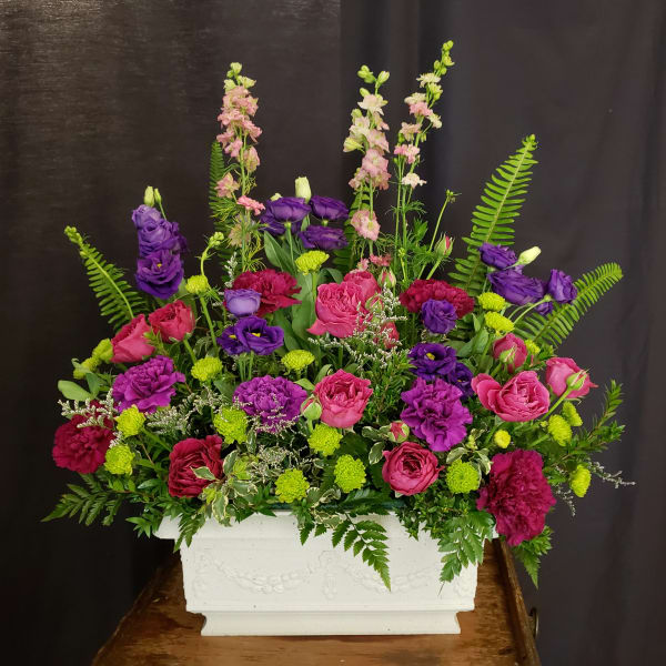 Pink and purple floral arrangement in a white rectangular planter