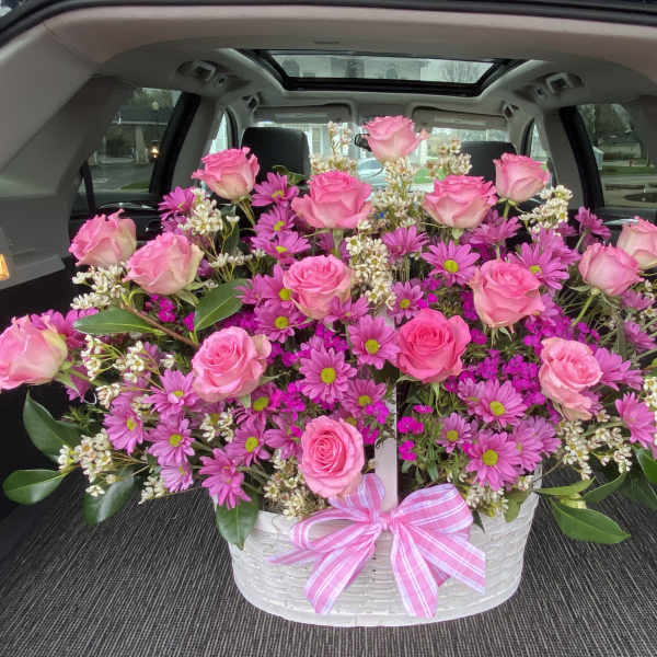 Pink roses and purple daisies arranged in a white basket with a pink ribbon