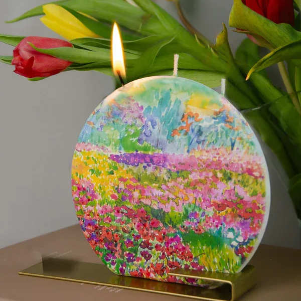 Tulips behind a colorful round candle with a lit wick