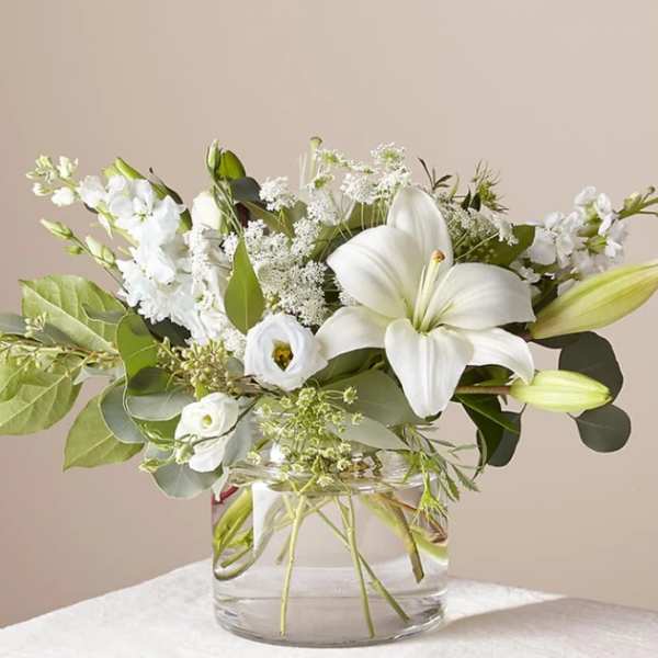 White lilies and mixed white flowers in a clear glass vase