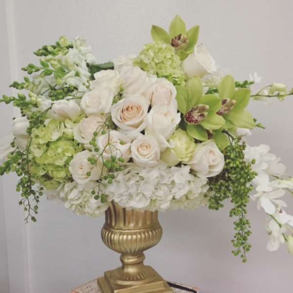 White and pale green floral arrangement in a gold urn vase