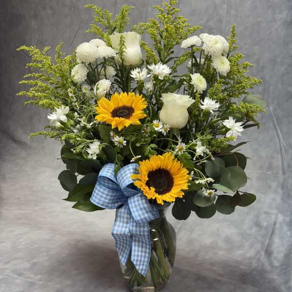 Sunflower and white rose bouquet in a glass vase with a blue ribbon