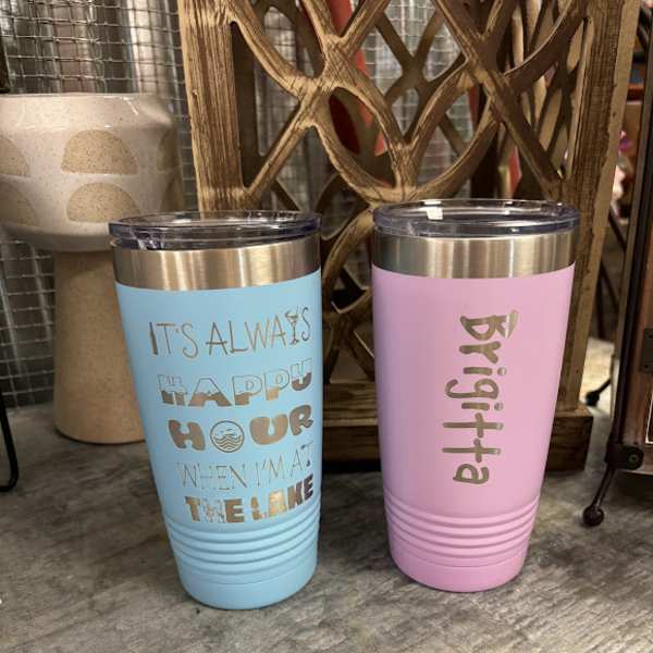 Two insulated tumblers with gold lids, one blue and one pink, with text on the front.