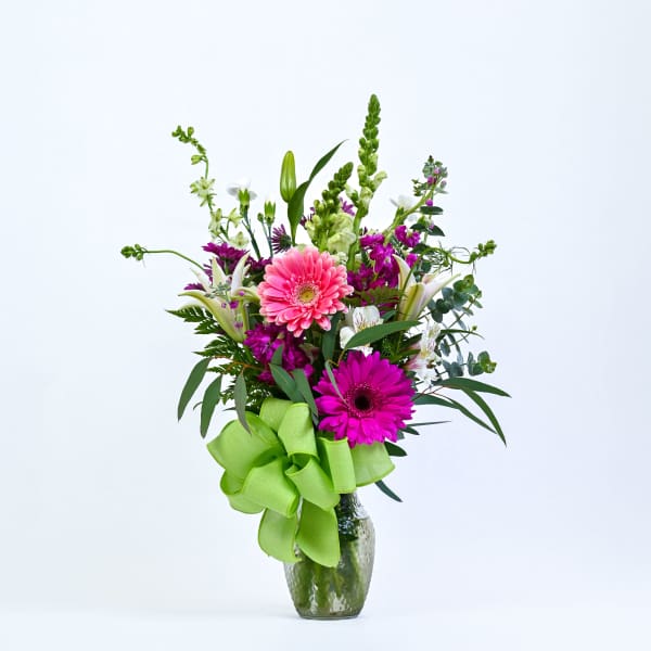 Pink and magenta gerbera bouquet in a glass vase with a green ribbon