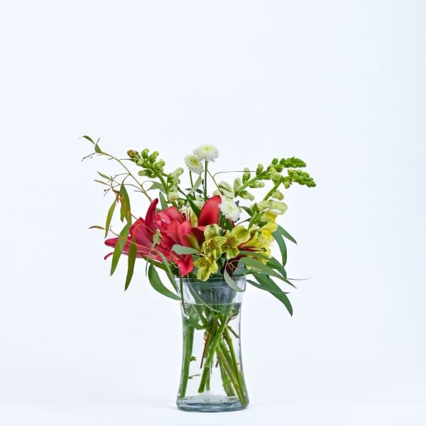 Mixed bouquet of pink lilies and green-yellow flowers in a clear glass vase